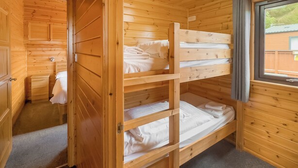 A wooden cabin room with bunk beds, a small dresser, and a window with a view. - Comfortable and spacious lodge with two doubles and one with bunks. (Glenluce, Newton Stewart)