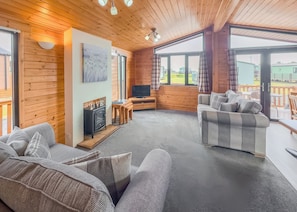 Ein gemütliches Blockhausschlafzimmer mit Kamin, Sofa, Fernseher und großen Fenstern mit Blick ins Freie.