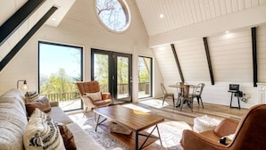 A spacious loft with a high ceiling, large windows, a dining area, and a cozy seating area.