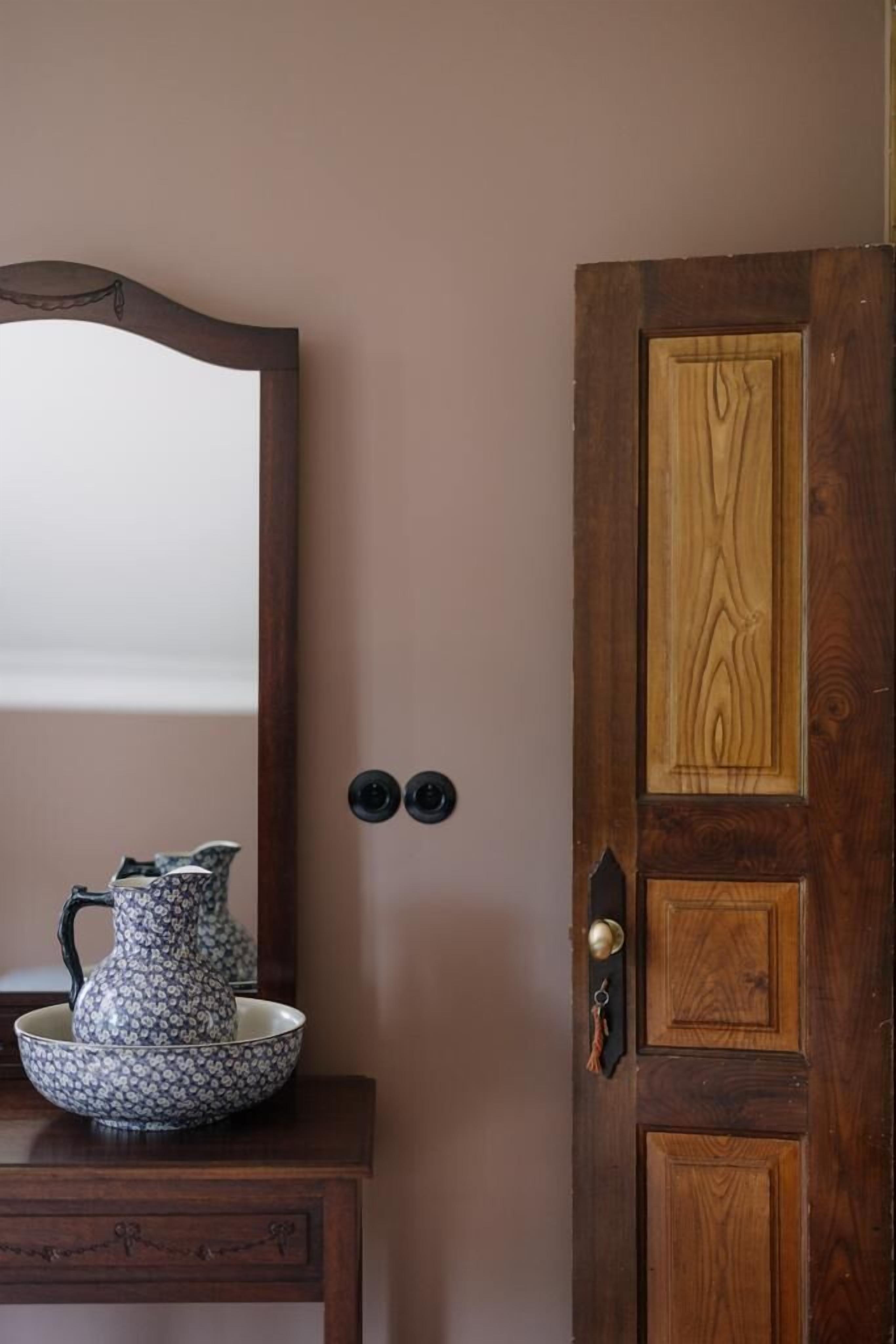 Een houten deur met een sleutelgat en een klein sleutelhanger, een spiegel met houten lijst en een decoratieve kruik op een houten tafel.