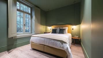 Une chambre avec un grand lit, une table de chevet, une petite table et une fenêtre avec des stores.