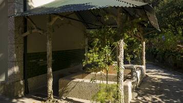 A covered outdoor area with a stone bench, a small tree, and a metal roof structure.
