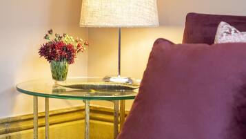 Une pièce avec une table en verre, une lampe, un vase de fleurs et un coussin violet.