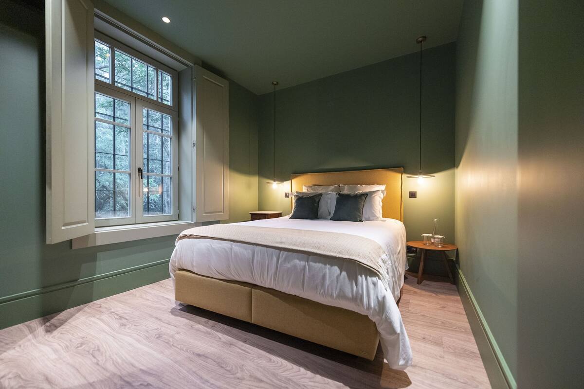 A bedroom with a large bed, a window, and a bedside table with a lamp.