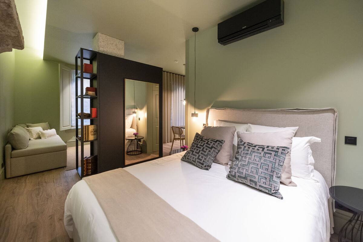 A hotel room with a bed, a sofa, a bookshelf, a mirror, and a desk.
