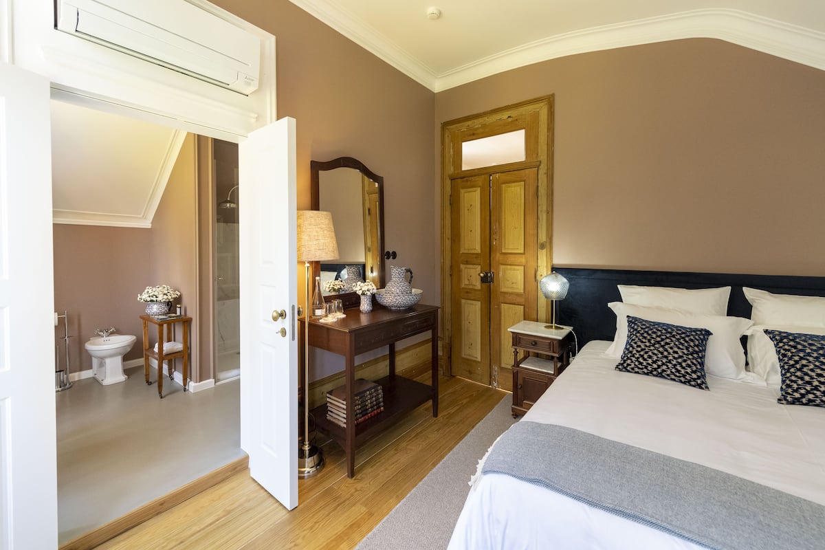 A bedroom with a bed, bedside table, lamp, dresser, and a door leading to a bathroom.