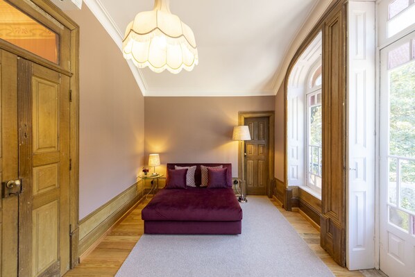 A bedroom with a large bed, wooden doors, a chandelier, and a view through the window.