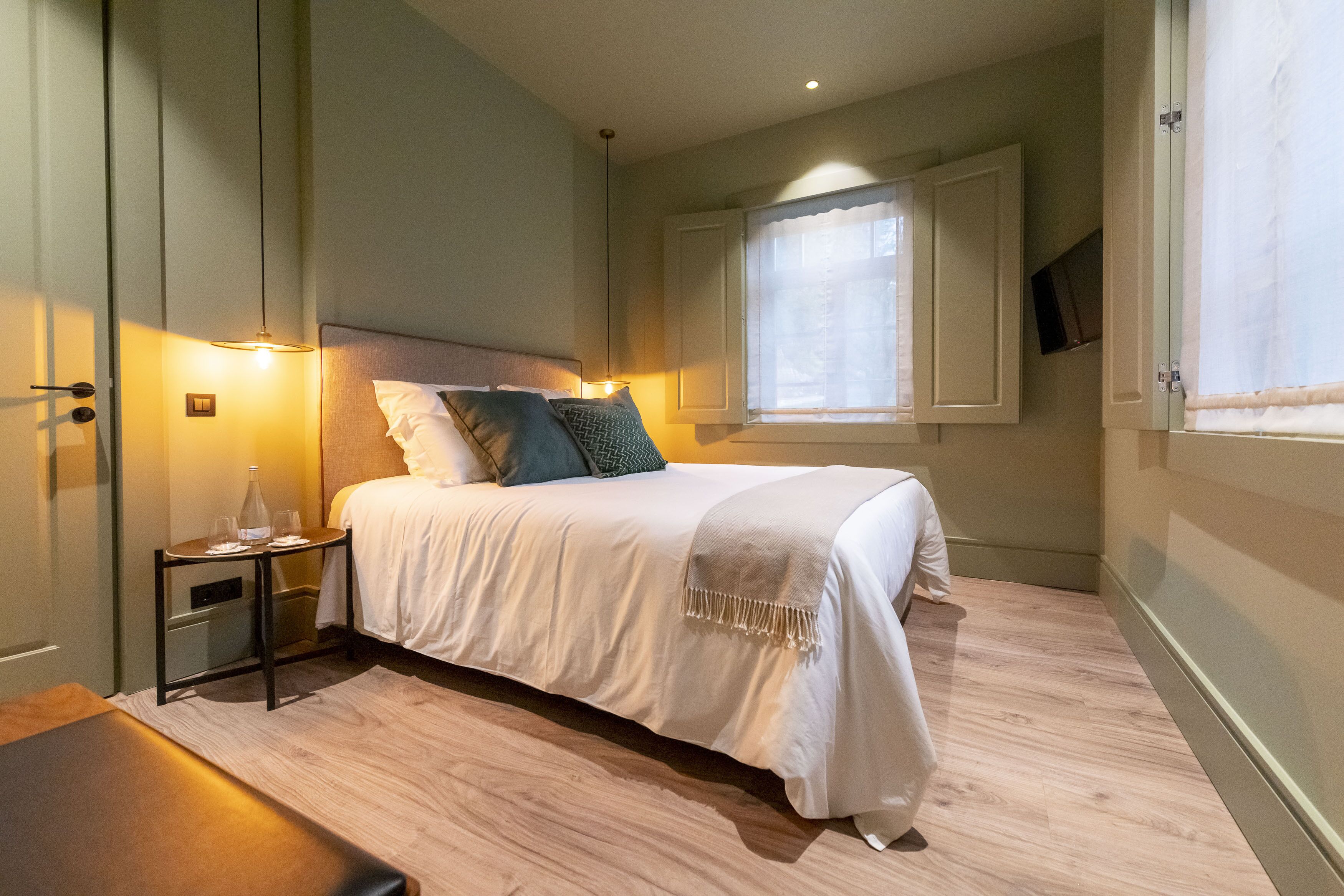 Un dormitorio ordenado con cama, mesita de noche y ventana con cortinas.
