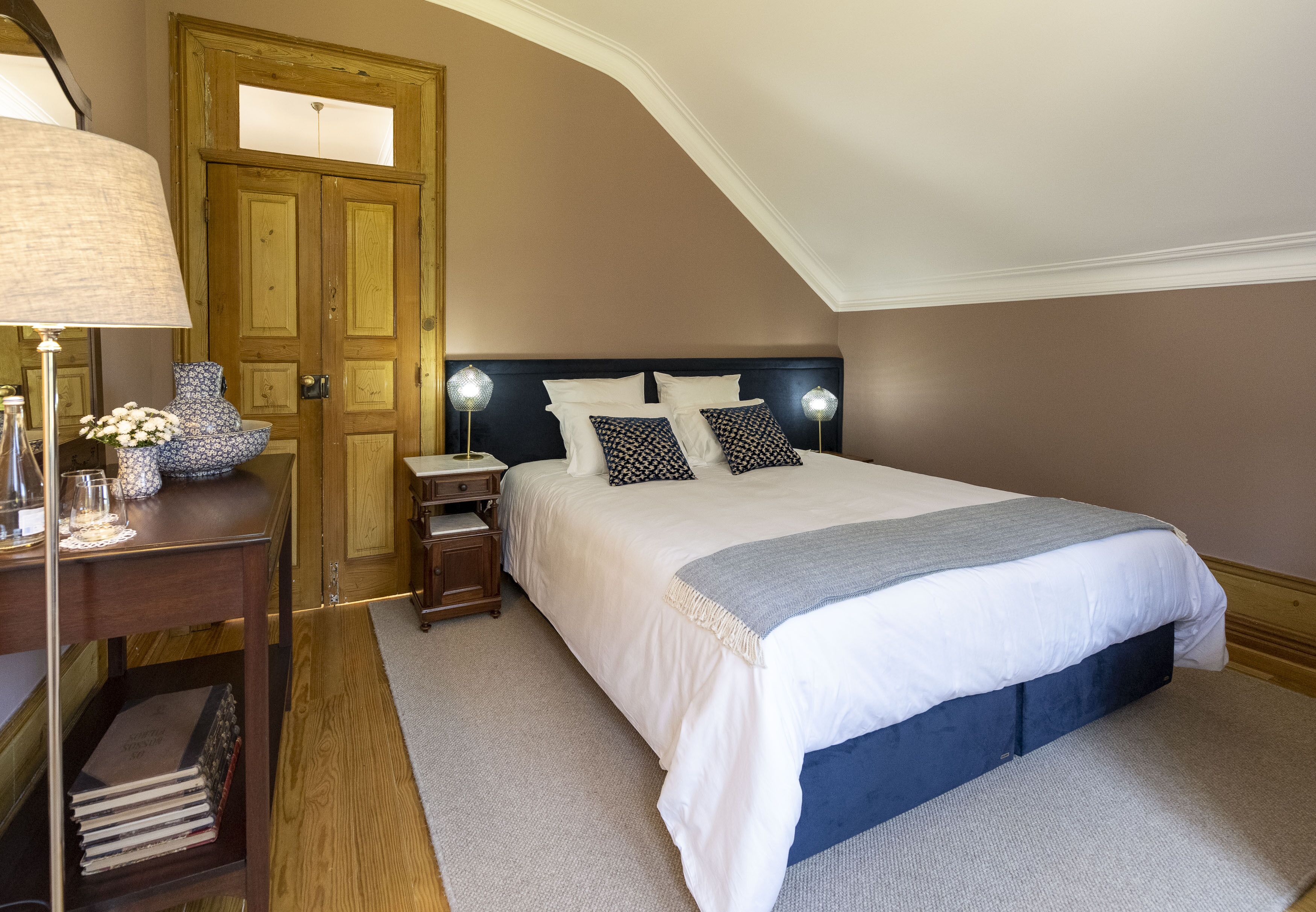 Un dormitorio con una cama grande, un armario de madera, un escritorio con una lámpara y una silla.
