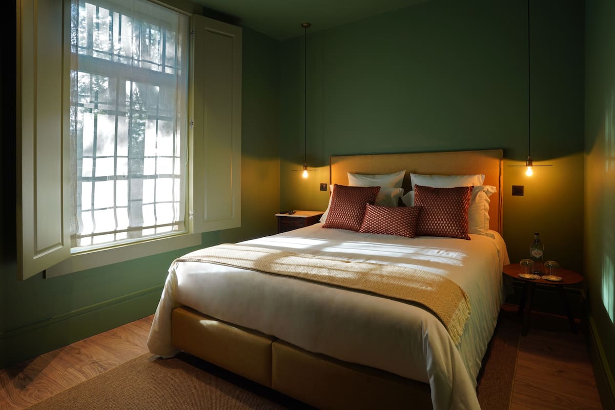 A bedroom with a large bed, a nightstand, a bedside table, and a window with curtains.