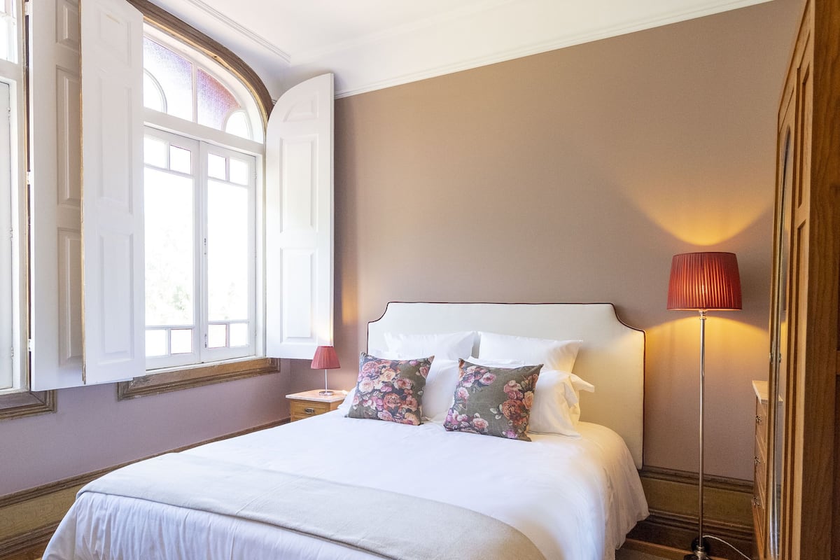 A bedroom with a large bed, a bedside lamp, and a window with curtains.