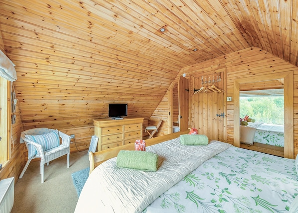 Une chambre dans un chalet en bois, avec un lit, une commode, une télévision et une fenêtre donnant sur un paysage agréable.