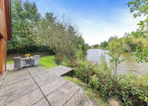 Un patio junto al río con mesa y sillas, una terraza de madera y vistas al río y al follaje.