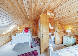 Un dormitorio de cabaña de madera con una cama, una mesita de noche, un aparador, un baño y un tragaluz.