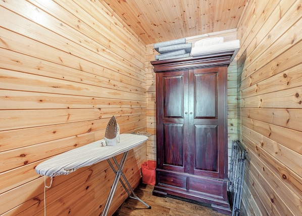 A wooden interior with a wooden wardrobe, an ironing board, and a red trash bin.