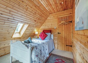 Une pièce aux murs lambrés, comprenant un lit, une table de chevet, une lampe, une porte et une fenêtre.