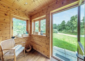 A wooden cabin with a bench, a basket, and a window with a view of a grassy area. - Ground floor: Spacious open plan lounge, kitchen, dining area with log burner. (Anglesey)