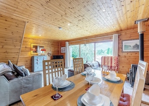 Interior de una cabaña de madera con una mesa de comedor, sillas, un sofá, un televisor y una chimenea.