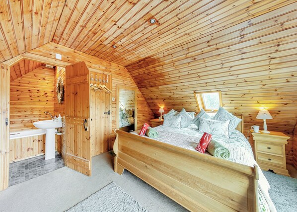 A wooden cabin bedroom with a bed, bedside tables, a mirror, and a sink.