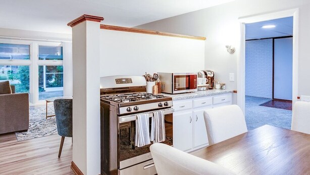 A modern kitchen with a gas stove, microwave, and white cabinets. There is a dining table with chairs and a view of a balcony.