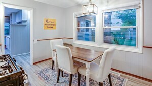 A dining area with a wooden table and white chairs, a rug, and a sign on the wall.