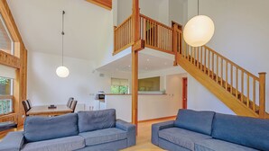 A spacious living area with two grey sofas, a wooden coffee table, a staircase with wooden railings, and a dining area in the background.