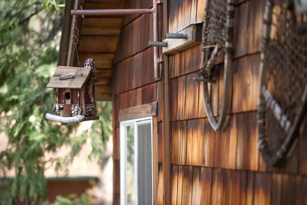 A wooden exterior with a birdhouse hanging from a metal rod.