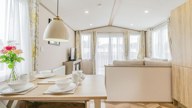 A modern hotel room with a dining area, a sofa, and a large window with curtains.