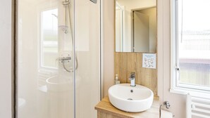 A modern bathroom with a glass shower enclosure, a wooden vanity with a sink, and a mirror above.