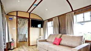 A cozy room with a beige sofa, a television, wooden flooring, and large windows.