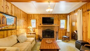 Una habitación acogedora con paredes de madera, chimenea, sofá, mesa de centro y televisor.
