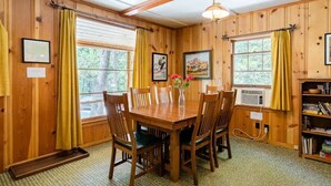 Un comedor de madera con una mesa y sillas, cuadros en las paredes y una estantería.