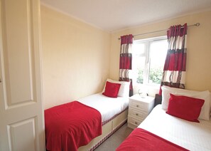 A bedroom with two beds, a nightstand, a window with curtains, and a door.