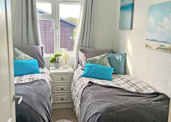 Une chambre double avec deux lits, une table de chevet avec une lampe, une petite plante et une fenêtre avec des stores.