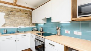 A modern kitchen with white cabinets, a stone wall, a blue tiled backsplash, and a built-in oven. - 2 bedroom accommodation in Watergate, Looe (Watergate, Looe)