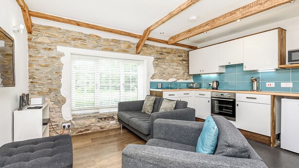 A modern kitchen with stone walls, wooden beams, and a grey sofa set. - 2 bedroom accommodation in Watergate, Looe (Watergate, Looe)