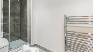 Ein modernes Badezimmer mit Duschkabine aus Glas, einer weißen Toilette und einem chromfarbenen Handtuchhalter.