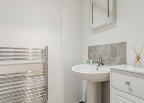 A modern bathroom with a chrome towel rack, a white sink, a marble backsplash, and a mirror.