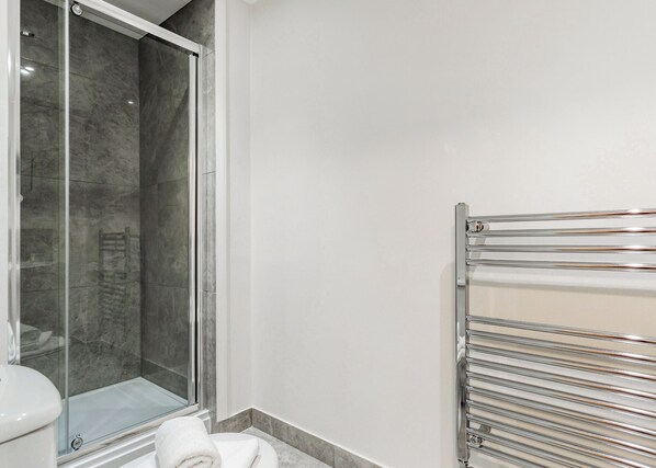 A modern bathroom with a glass shower enclosure, a white toilet, and a chrome towel rack.