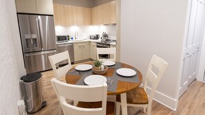 A modern kitchen with stainless steel appliances, wooden cabinets, and a dining area with a round table set for four. - Spacious, DWNT/OTR condo. minutes walk to the Reds/Bengals stadiums & more!! (Cincinnati)
