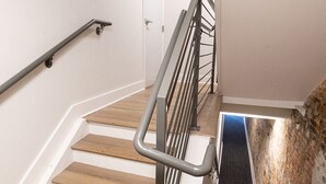 A wooden staircase with a metal handrail and a glass panel on the right. - Spacious, DWNT/OTR condo. minutes walk to the Reds/Bengals stadiums & more!! (Cincinnati)