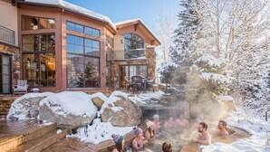 Ett spaområde med bubbelpooler och en pool omgiven av sten, inbäddat bland snötäckta klippor och träd.