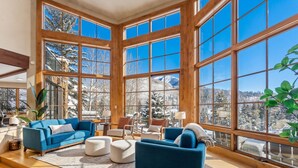 A spacious room with large windows, a blue sofa, a white ottoman, and a wooden floor. - Star Mountain Lodge💎23 Guests🏔️Grotto Waterfall🌊Theater🍿Game room🧖‍♀️Spa (Keystone)