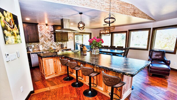 A kitchen with a large island, bar stools, and a dining area with a chair. - Large Cabin Hot tub, Sauna, Fire Pit, BBQ, 2 Decks, Updated Kitchen (McCall)