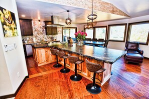 A kitchen with a large island, bar stools, and a dining area with a chair. - McCall Lodge Sleeps 19 | Hot Tub + Sauna | 2.5 Hrs from Boise | Near Lake (McCall)