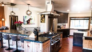 A spacious kitchen with a central island, bar stools, stainless steel appliances, and a large window providing natural light. - Large Cabin Hot tub, Sauna, Fire Pit, BBQ, 2 Decks, Updated Kitchen (McCall)