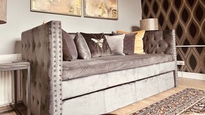 Un canapé gris à motifs avec des clous métalliques, un tapis à motifs et des œuvres d’art abstraites accrochées au mur.