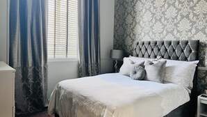 Un lit bien fait, avec une tête de lit capitonnée, une lampe de chevet et un papier peint à motifs.
