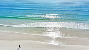 Ein Strand mit klarem Wasser, einem sandigen Ufer und einigen Personen.