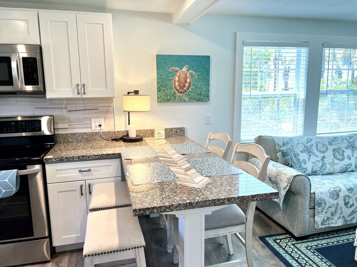 A modern kitchen with white cabinets, a granite countertop, and a dining area with a table and chairs.